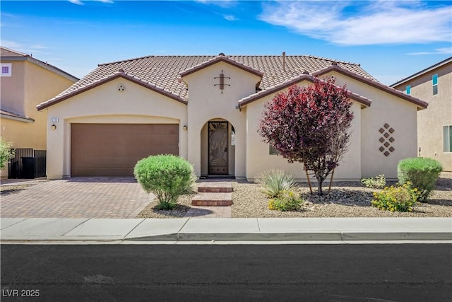 mediterranean / spanish-style home with a tile roof, a garage, stucco siding, and decorative driveway