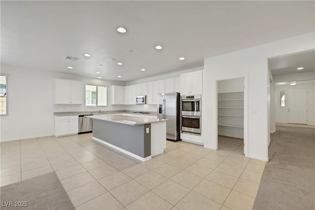 kitchen with appliances with stainless steel finishes, light tile patterned flooring, a kitchen island, white cabinets, and recessed lighting