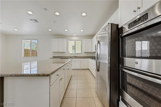 kitchen featuring stainless steel appliances, recessed lighting, light stone counters, a center island, and light tile patterned floors