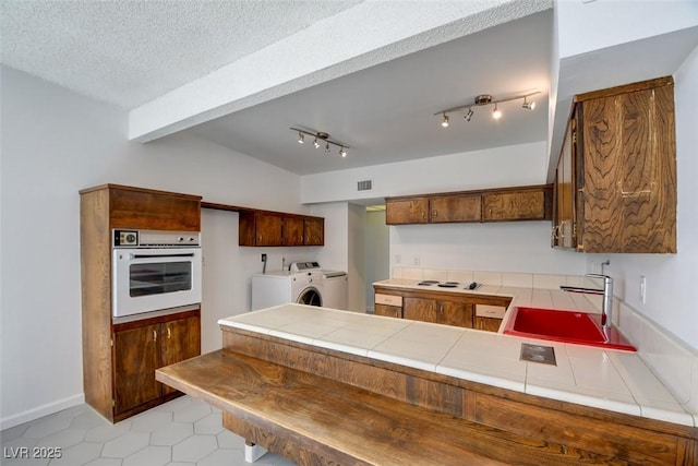 kitchen with white appliances, a sink, separate washer and dryer, tile countertops, and a peninsula