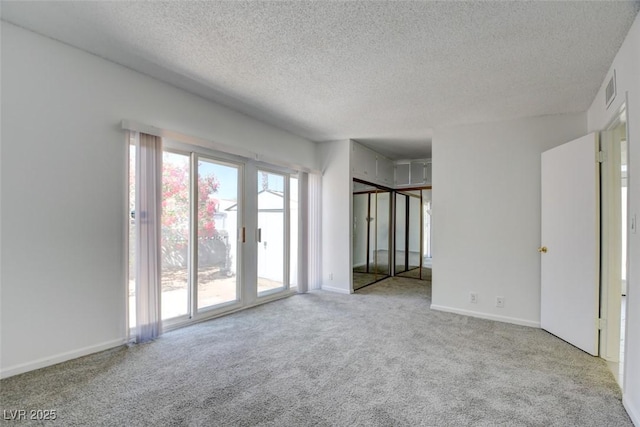 carpeted spare room with a textured ceiling and baseboards