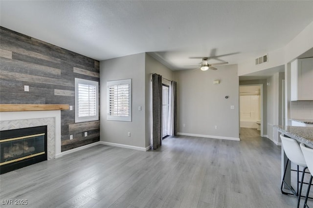 unfurnished living room with an accent wall, wood walls, light wood finished floors, ceiling fan, and a tile fireplace