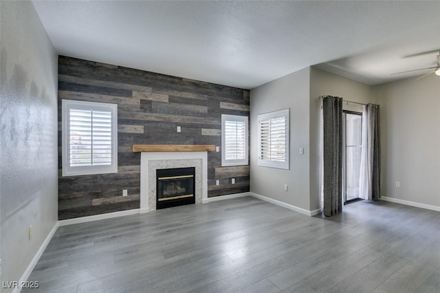 unfurnished living room with an accent wall, a glass covered fireplace, baseboards, and wood walls