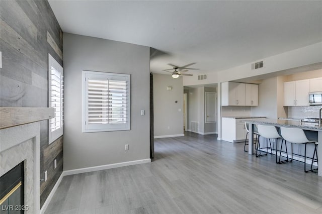 living area featuring ceiling fan, light wood-style floors, a premium fireplace, and baseboards