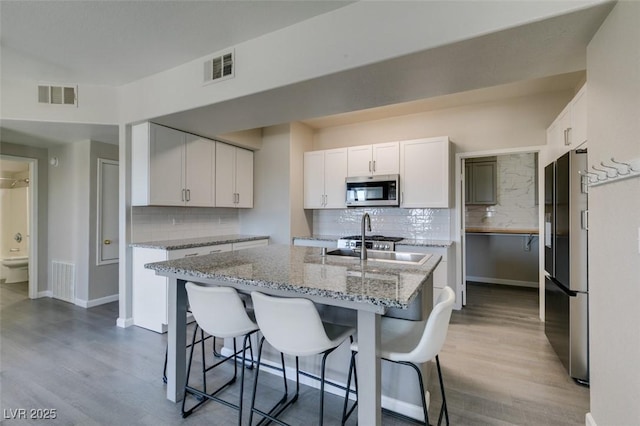 kitchen with appliances with stainless steel finishes, backsplash, white cabinets, and wood finished floors