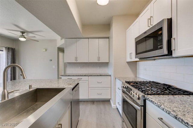 kitchen with appliances with stainless steel finishes, a sink, white cabinets, light wood-type flooring, and a ceiling fan
