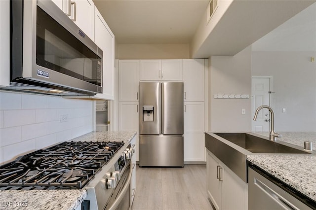 kitchen with stainless steel appliances, a sink, light wood-style floors, white cabinetry, and light stone counters