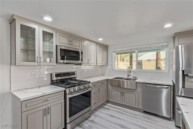 326 Fuente Dr, Henderson, NV 89014 - kitchen featuring stainless steel appliances, a sink, gray cabinetry, light stone counters, and light wood finished floors