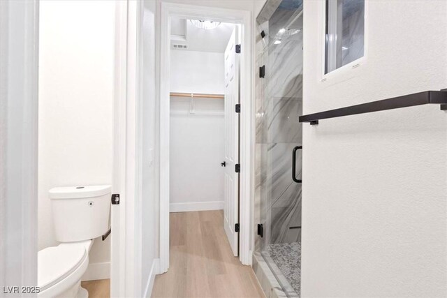 full bath with a shower stall, wood finished floors, toilet, baseboards, and a walk in closet
