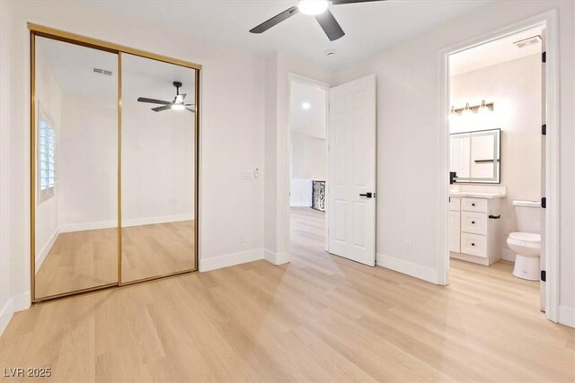 unfurnished bedroom with light wood-style flooring, ensuite bath, baseboards, a closet, and a ceiling fan