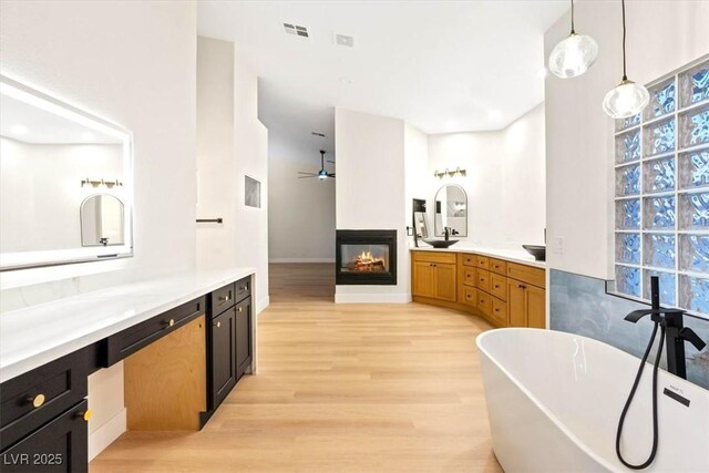 full bathroom with ceiling fan, a multi sided fireplace, wood finished floors, a freestanding tub, and vanity