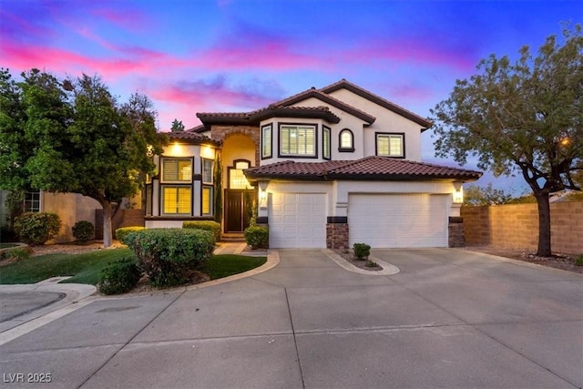mediterranean / spanish home featuring driveway, a garage, fence, stucco siding, and a tiled roof
