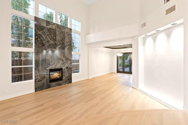 unfurnished living room with wood finished floors, a tile fireplace, a towering ceiling, and baseboards