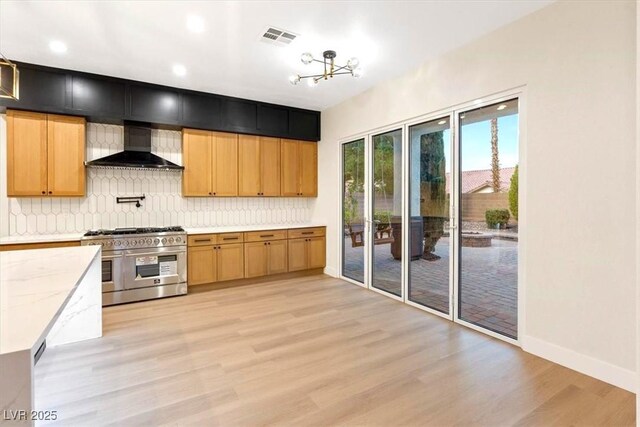 kitchen with range with two ovens, wall chimney exhaust hood, light wood-style flooring, decorative backsplash, and light stone countertops