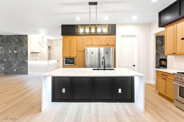 kitchen with stainless steel appliances, light wood-style floors, an island with sink, tasteful backsplash, and light stone counters