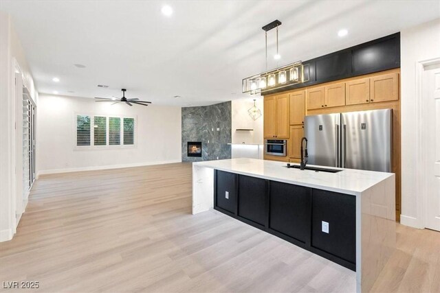 kitchen featuring high end fridge, a sink, a ceiling fan, light wood-style floors, and baseboards