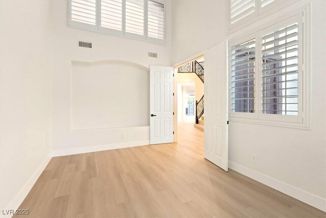 unfurnished room featuring light wood finished floors, baseboards, healthy amount of natural light, and a towering ceiling
