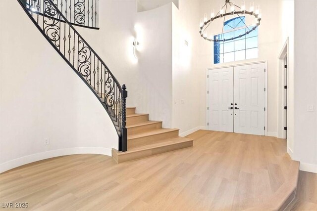 foyer with a towering ceiling, a chandelier, baseboards, stairs, and wood finished floors