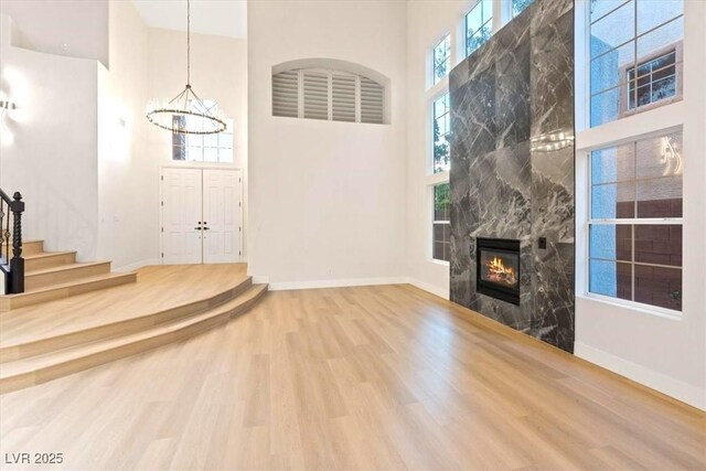 unfurnished living room featuring a high ceiling, wood finished floors, a chandelier, stairway, and baseboards