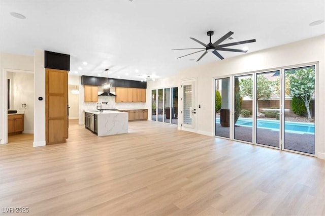 unfurnished living room featuring light wood finished floors, a ceiling fan, baseboards, a sink, and recessed lighting
