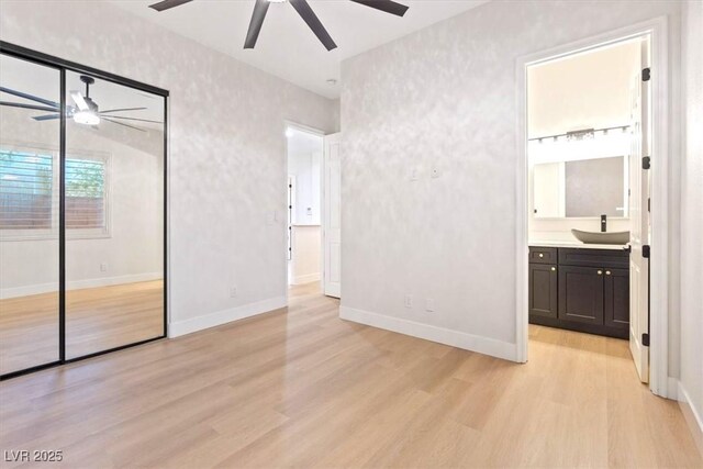 unfurnished bedroom featuring a sink, light wood-type flooring, baseboards, and a closet