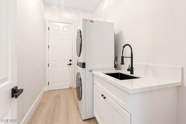 clothes washing area with stacked washer and clothes dryer, cabinet space, light wood finished floors, and baseboards