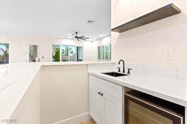 kitchen with a sink, beverage cooler, light stone counters, white cabinetry, and baseboards