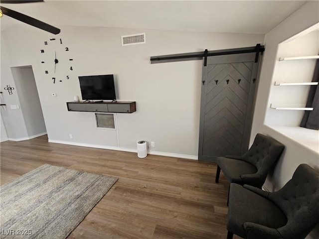 living area featuring vaulted ceiling, wood finished floors, a ceiling fan, a barn door, and baseboards
