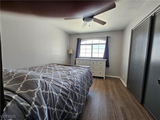 bedroom featuring dark wood finished floors, a ceiling fan, baseboards, and a closet