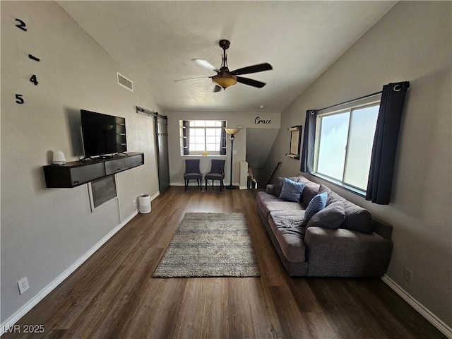 living room featuring lofted ceiling, ceiling fan, a barn door, wood finished floors, and baseboards