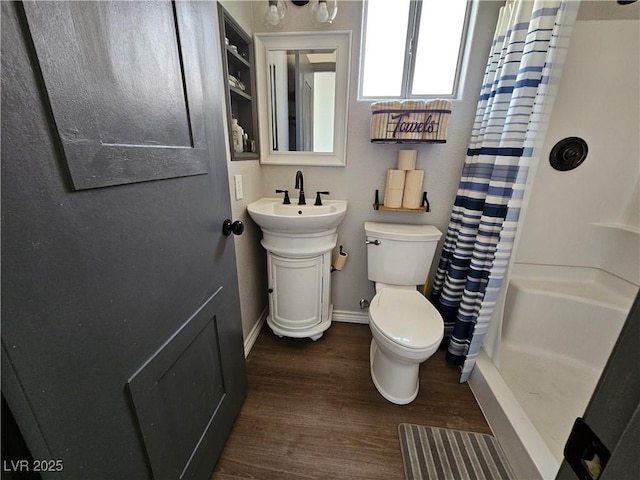 bathroom with curtained shower, wood finished floors, baseboards, toilet, and a sink