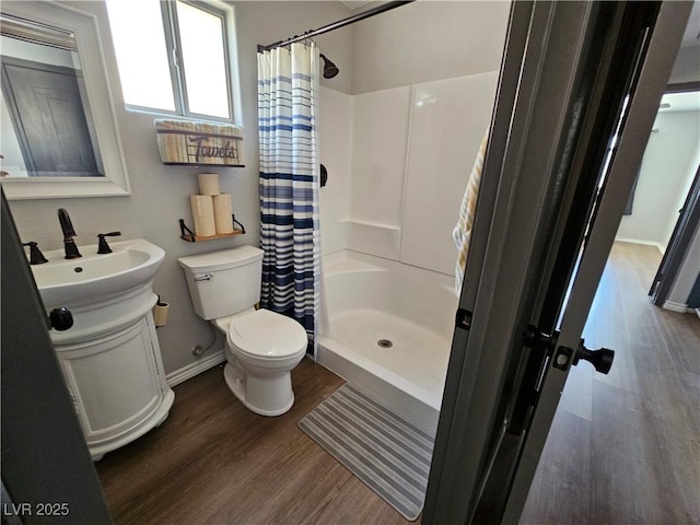bathroom featuring wood finished floors, a shower stall, toilet, baseboards, and vanity