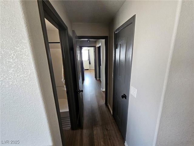 hallway featuring dark wood-style flooring, baseboards, and a textured wall