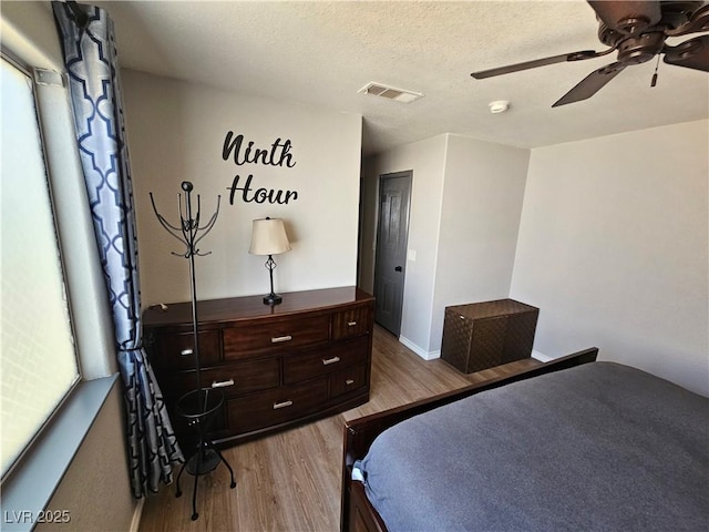 bedroom with light wood-style flooring, ceiling fan, baseboards, and a textured ceiling