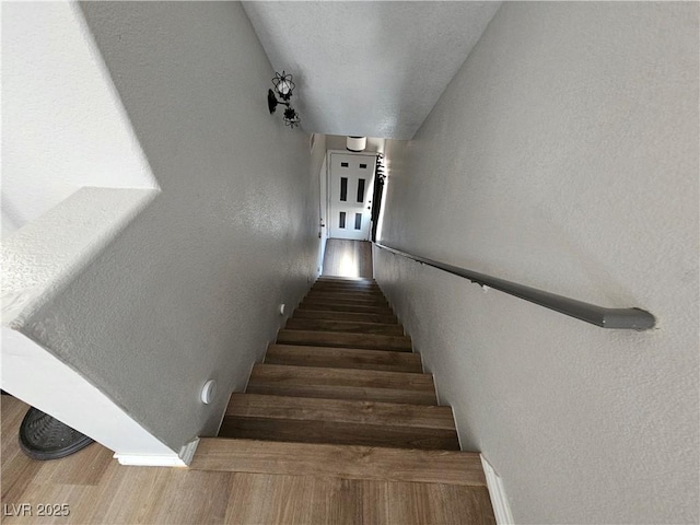stairway featuring a textured wall, wood finished floors, and baseboards