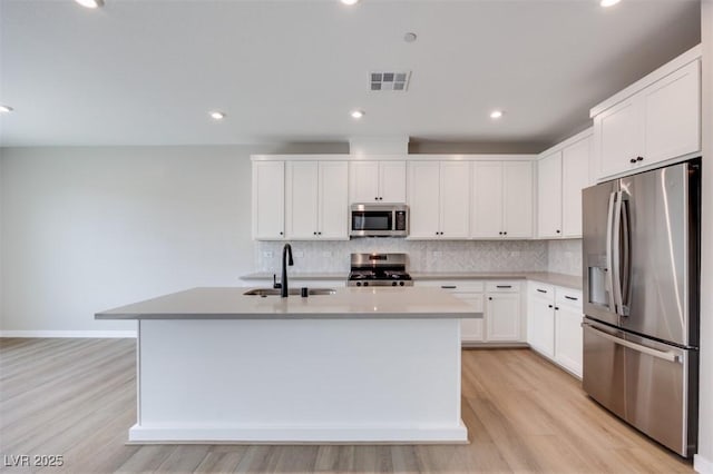 kitchen featuring appliances with stainless steel finishes, a sink, light wood-style flooring, backsplash, and recessed lighting