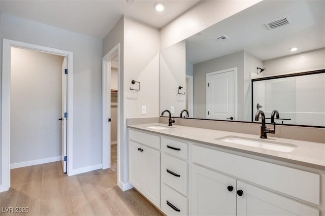 full bathroom featuring a stall shower, wood finished floors, double vanity, baseboards, and a spacious closet