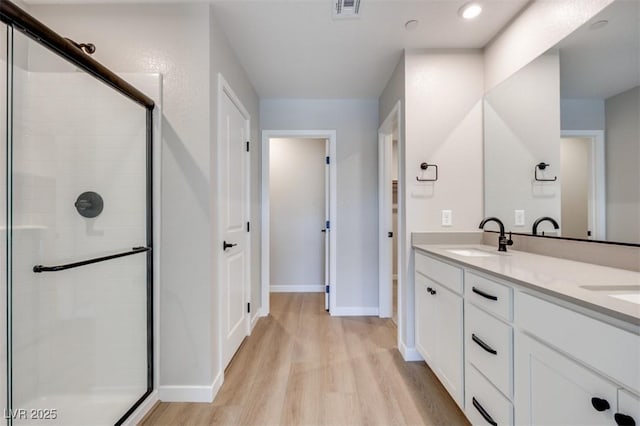 full bathroom with wood finished floors, a stall shower, baseboards, and double vanity