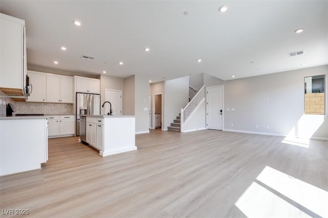 kitchen featuring tasteful backsplash, a center island with sink, light wood-style flooring, open floor plan, and a sink
