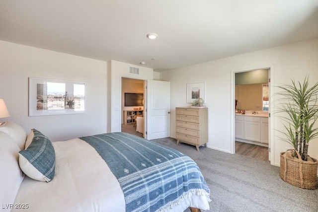 bedroom with light carpet, ensuite bath, and baseboards