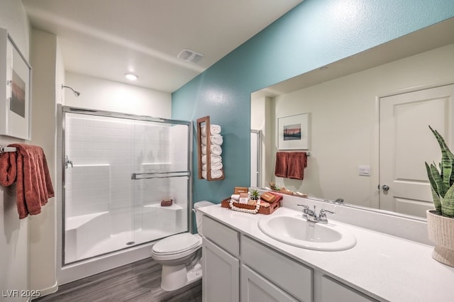 bathroom with wood finished floors, a shower stall, toilet, and vanity
