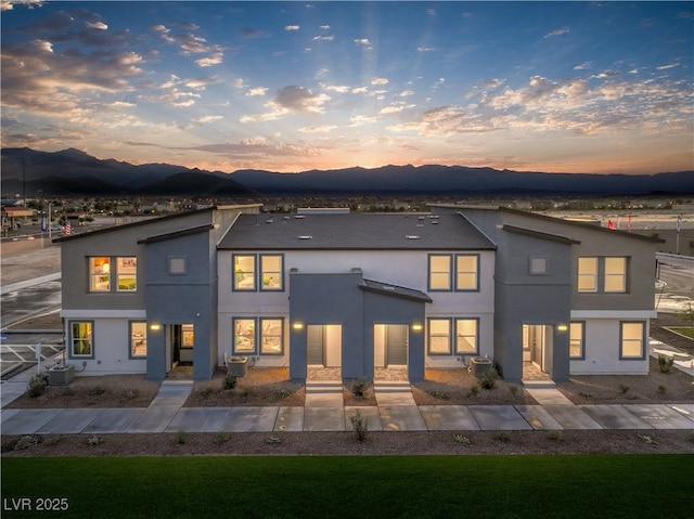 back of property at dusk featuring a mountain view, central AC, and stucco siding