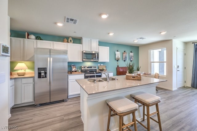 kitchen with stainless steel appliances, a sink, light wood finished floors, a breakfast bar, and recessed lighting
