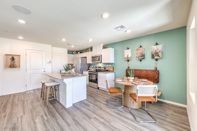 kitchen featuring stainless steel appliances, white cabinets, a kitchen island with sink, light wood finished floors, and recessed lighting