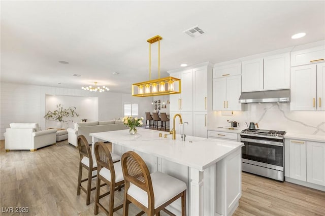 9615 Sedona Hills Ct, Las Vegas, NV 89147 - kitchen with stainless steel gas range, under cabinet range hood, open floor plan, light wood-style floors, and a kitchen bar