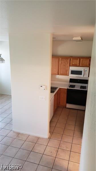kitchen with range, white microwave, light tile patterned flooring, light countertops, and a sink