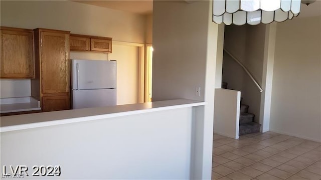 kitchen featuring freestanding refrigerator, light tile patterned floors, a peninsula, brown cabinetry, and light countertops