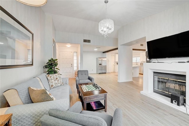 6771 Shelter Ln, Las Vegas, NV 89103 - living area featuring light wood-style flooring, a chandelier, and a glass covered fireplace