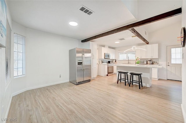 6771 Shelter Ln, Las Vegas, NV 89103 - kitchen featuring appliances with stainless steel finishes, light wood-style floors, beam ceiling, a kitchen bar, and a kitchen island