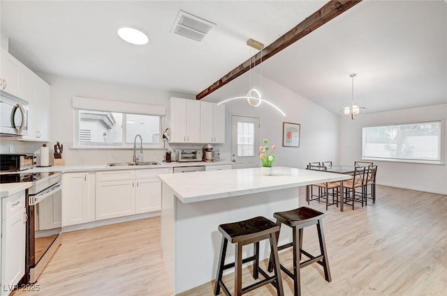 6771 Shelter Ln, Las Vegas, NV 89103 - kitchen with a sink, stainless steel appliances, light wood finished floors, a breakfast bar area, and white cabinetry